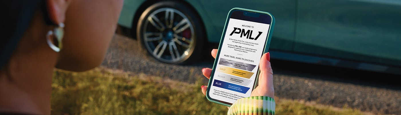 A PML ONE member viewing her membership on the OneGo app beside her BMW.